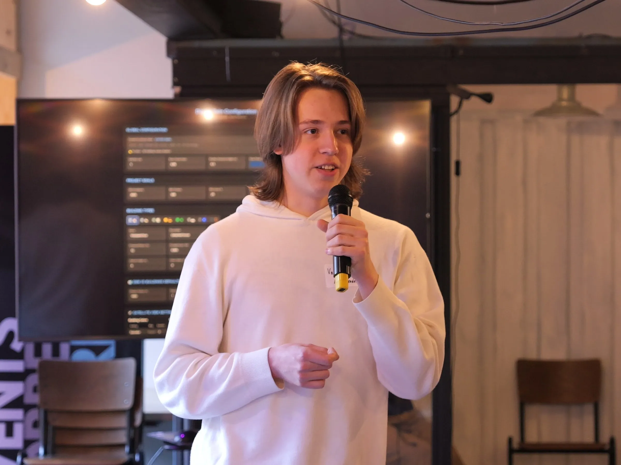Valerii speaking into a microphone in front of a large screen showing the application's project configuration screen